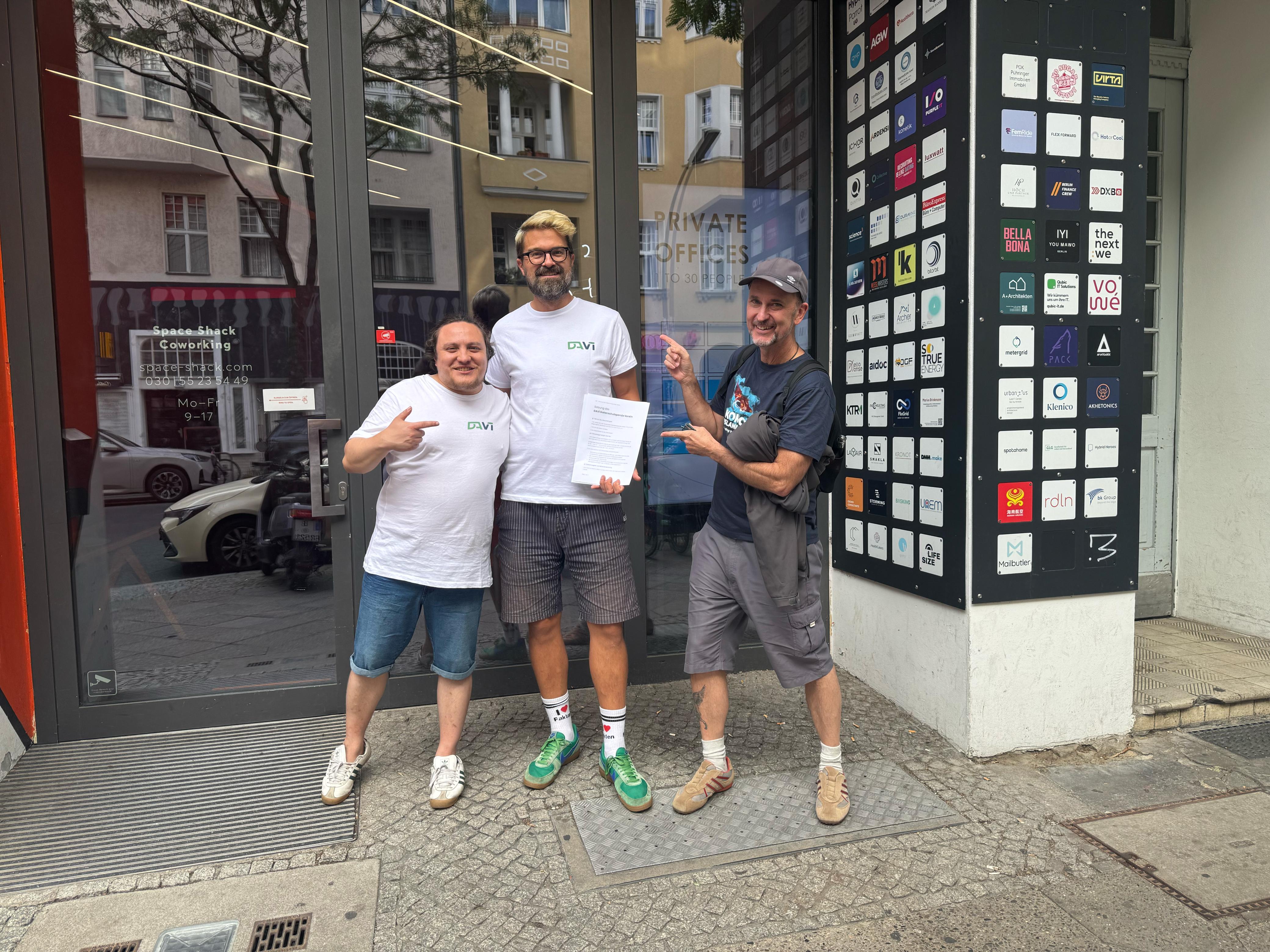 Gründungstag: drei Männer stehen gut gelaunt vor dem Space Shack Coworking in Berlin, zwei davon in weißen DAVi-T-Shirts; der mittlere hält die unterschriebene Vereinssatzung.